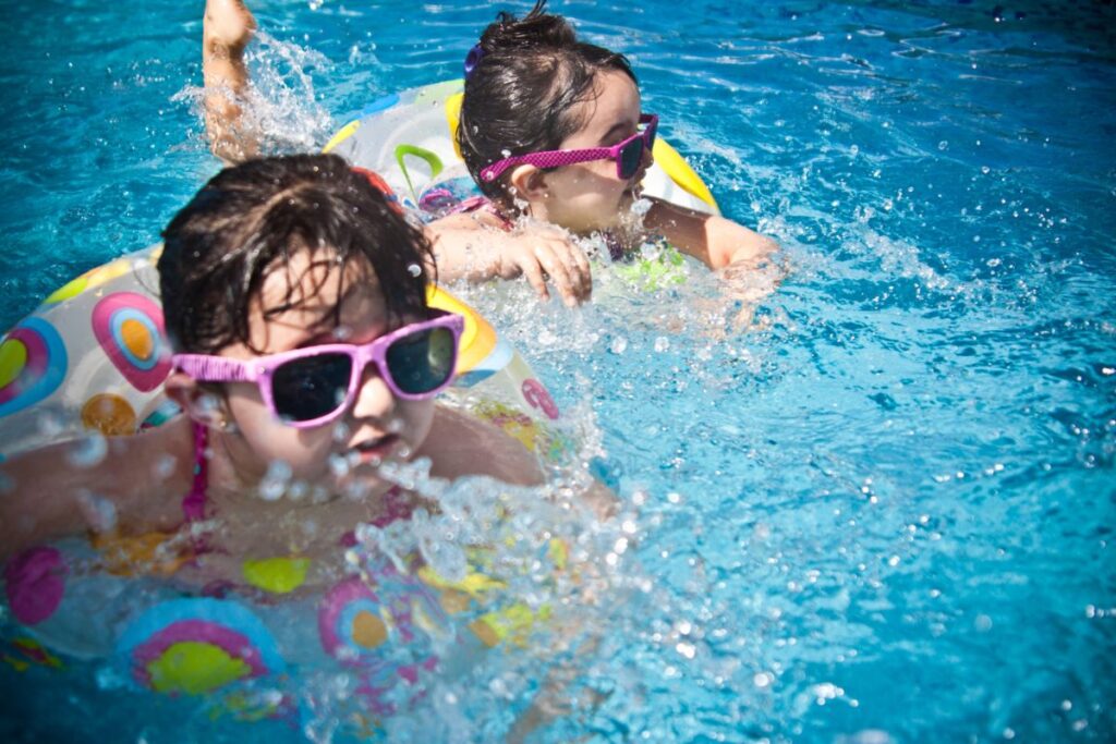 an image of two young children playing in a pool with sun glasses and flotation devices